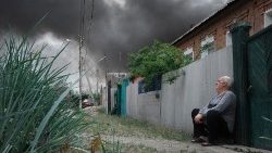 खार्किव में रूसी हमले से उठते धुंए के निकट, अपने घर के बाहर बैठा एक आदमी