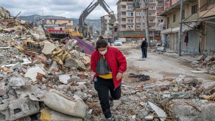 A woman walks on the rubble of a collapsed building in southeast Türkiye