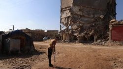 O sobrevivente do terremoto sírio, Hamza Al-Ahmed, passa por prédios destruídos no campo onde mora, na cidade de Jindayris, no noroeste da província de Aleppo, em 4 de fevereiro de 2024. (Foto de Aaref WATAD/AFP)