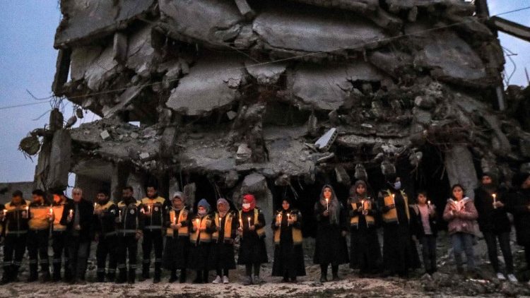 Members of the Syrian Civil Defence stand in a candle-lit remembrance vigil with survivors of the February 6, 2023 earthquake