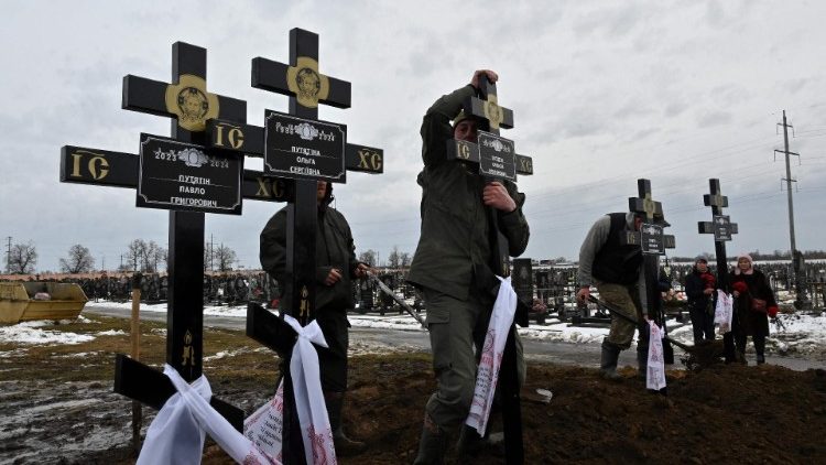 Funcionários de cemitério cravam cruzes junto aos túmulos de família de 5 pessoas, incluindo 3 crianças, mortas em ataque russo com drone em Karkiv, 12 de fevereiro de 2024. (Photo by Sergey Bobok/AFP)