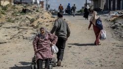 Um homem puxa uma mulher palestina idosa em uma cadeira de rodas em meio ao conflito entre Israel e o Hamas (AFP)