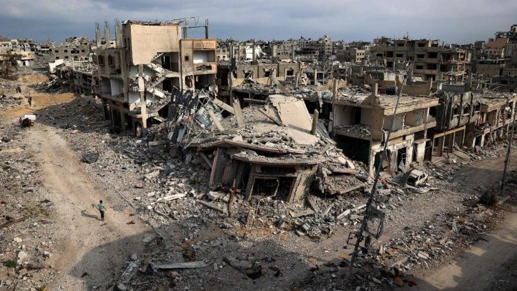 Palestinos passam por prédios destruídos em Khan Yunis, depois que Israel retirou suas forças terrestres do sul da Faixa de Gaza (AFP)