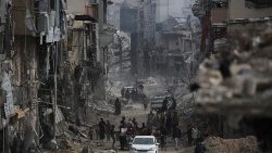 Palestinos passam por prédios danificados em Khan Yunis em 8 de abril de 2024, seis meses após guerra devastadora (AFP)