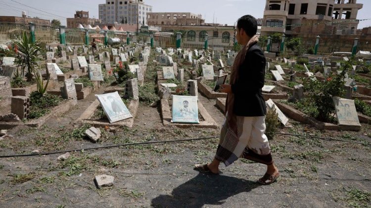 A man walks past portraits on the graves of war victims at a cemetery in Sana'a