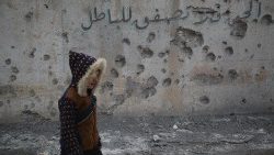 Jovem passa por um muro onde se lê: 'Se você não pode dizer a verdade, não aplauda a falsidade', depois que bombas caíram em uma área residencial, na cidade de Daret Azzah, zona rural de Aleppo, Síria, 1º de janeiro de 2024.  (EPA/BILAL AL-HAMMOUD)