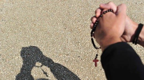 A boy who recites the 'Our Father' prayer with a rosary in his hand casts a shadow, after Pope ...