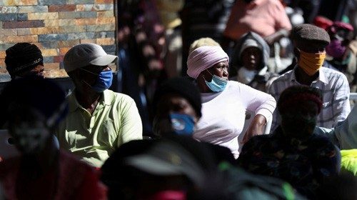 Men and women sit in a queue waiting for government grants as South Africa starts to relax some ...