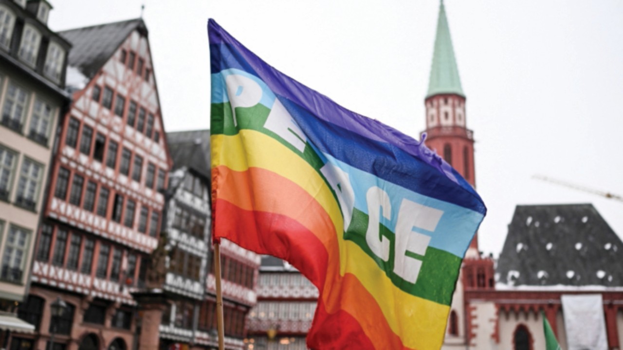 A rainbow colored flag with the inscription 'Peace' flutters in the wind during a demonstration ...