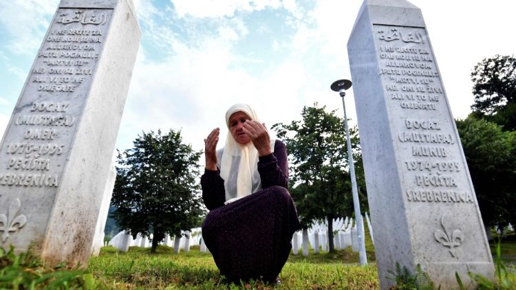 A Bosnian Muslim woman prays between the tombstones of her sons who were killed during the Srebrenica massacre in 1995