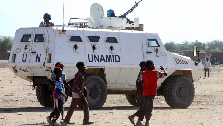 Sudanese children walk past an amoured vehicle of the UN-AU peacekeeping mission in Darfur