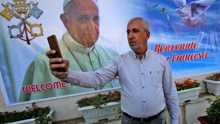 An Iraqi citizen takes a "selfie" against a banner welcoming Pope Francis