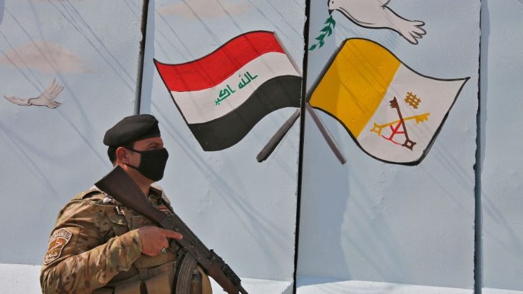 Segurança armado caminha perto de um pôster do Papa Francisco alusivo a sua viagem ao Iraque, em Bagdá