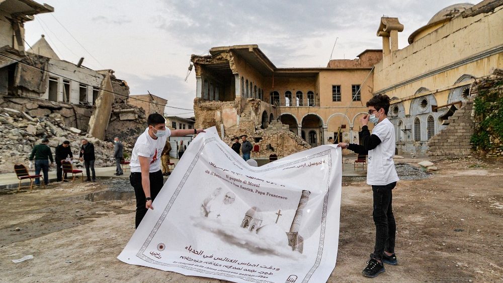 Jóvenes despliegan un cartel de bienvenida al Papa Francisco en las ruinas de la iglesia católica siria de la Inmaculada Concepción en Iraq.