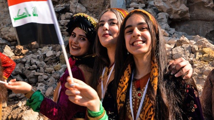 (file photo) Young women dressed in traditional clothing wave an Iraqi national flag during Pope Francis 2021 visit to Iraq