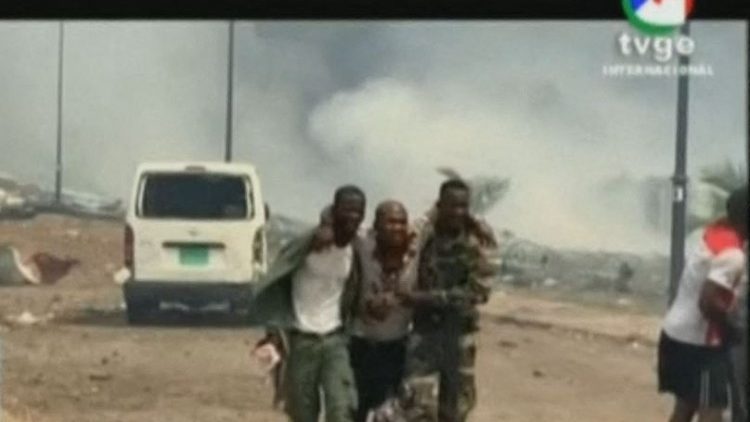 Screenshot of TVGE shows soldiers assisting a wounded man in Bata, as smoke rises in the background