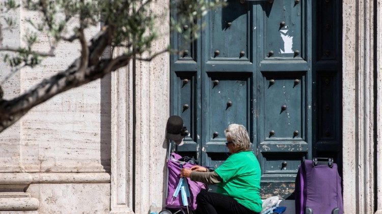 A homeless woman fixes face masks on her cart as she sits on the steps of a church in Rome, 7 April 2021
