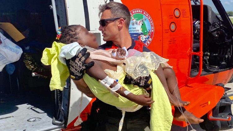 Na tomto snímku s laskavým svolením americké pobřežní stráže je vidět, jak člen posádky letecké pobřežní stráže pomáhá přepravit kriticky zraněné dítě z vrtulníku do čekající záchranné služby v Port au Prince na Haiti, 15. srpna 2021.