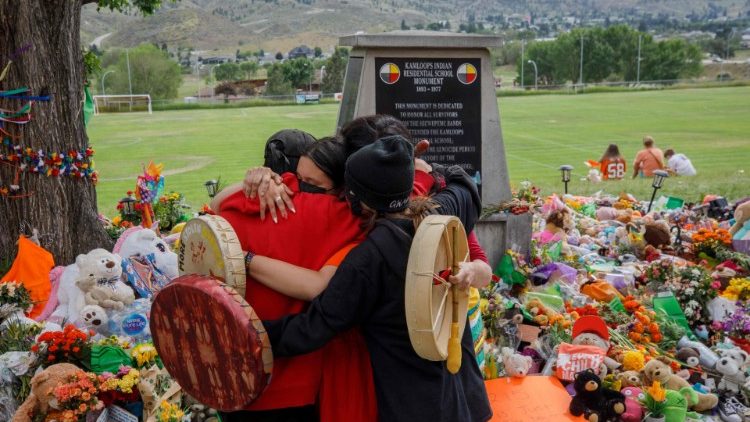 People hug in front of a temporary monument at the former Kamloops Indian Residential School (June 2021)
