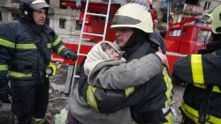 Un Vigile del Fuoco ucraino abbraccia una anziana donna soccorsa a Kiev (Afp)
