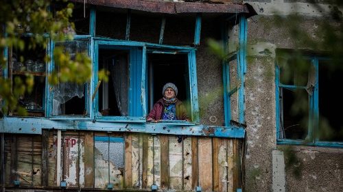 An elderly woman stands of the balcony of her damaged home following a shelling on the town of Bakhut in Donetsk