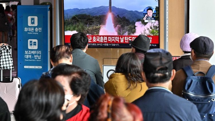 People in a Seoul railway station watch a television screen showing a news broadcast with file footage of a North Korean missile test.