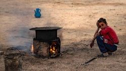 A Syrian boy squats by a makeshift stove at the Sahlah al-Banat camp for displaced people, near Raqa, Syria