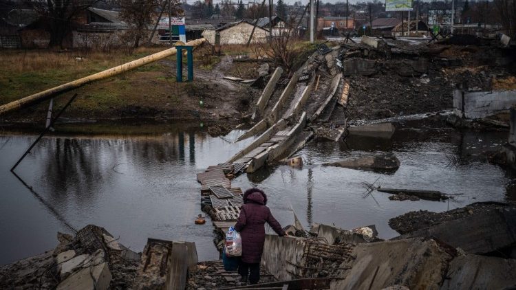Uma mulher atravessa uma ponte destruída em Bakhmut, região de Donetsk, em 6 de janeiro de 2023, em meio à invasão russa da Ucrânia. - A Rússia e a Ucrânia sofreram pesadas baixas na luta por Bakhmut, e a maior parte da população pré-guerra da cidade de 70.000 habitantes partiu para um território mais seguro, deixando para trás estradas cheias de crateras e edifícios reduzidos a escombros e metal retorcido. (Foto de Dimitar DILKOFF / AFP)
