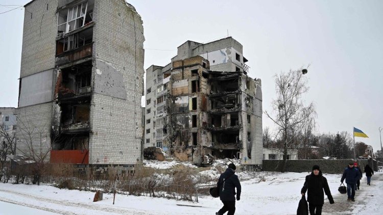 Ucranianos caminham diante de prédios destruídos em Borodyanska, em 12 de janeiro de 2022. AFP/Sergei SUPINSKY
