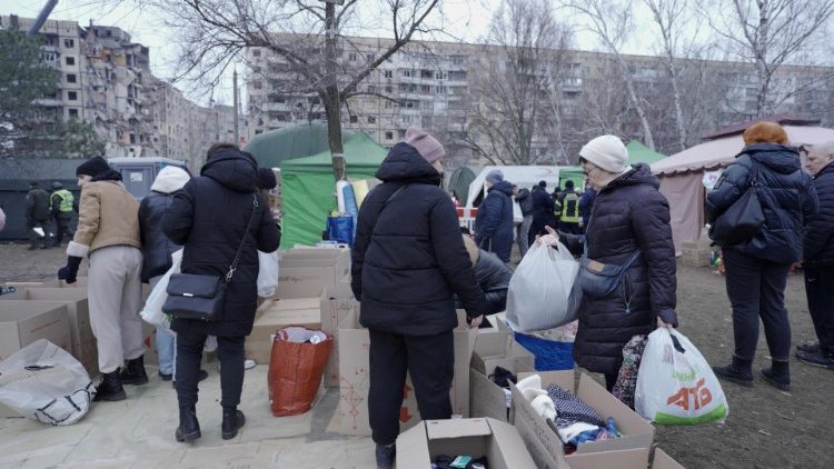 Ucranianos trazem ajuda, tendo ao fundo do prédio bombardeado em Dnipro