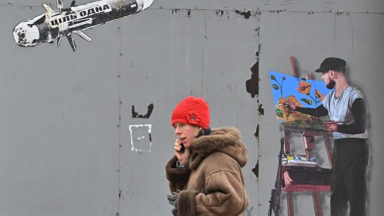 Ucraniana fala em um telefone celular enquanto passa por um mural representando um míssil voador e um artista em seu cavalete, no centro da capital ucraniana de Kyiv em 30 de janeiro de 2023, em meio à invasão russa da Ucrânia. (Foto de Sergei SUPINSKY / AFP)