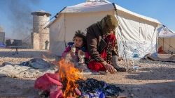 Sírios se aquecem em um incêndio em um abrigo improvisado para pessoas que ficaram desabrigadas, perto da cidade de Jindayris, controlada pelos rebeldes, em 8 de fevereiro de 2023, dois dias após um terremoto mortal atingir a Turquia e a Síria. (Foto de Rami al SAYED/AFP)