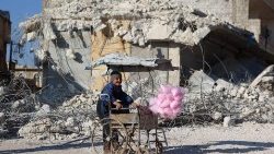 Uma criança síria que vende algodão doce sorri em frente aos escombros de um prédio que desabou após o terremoto da semana passada no vilarejo de Atarib, controlado por rebeldes na Síria, na província de Aleppo, no noroeste, em 14 de fevereiro de 2023. (Photo by Aaref WATAD / AFP)