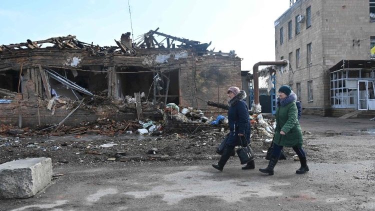 Mulheres passam por fábrica de processamento de carne destruída por bombardeios russos em Vovchans'k, região de Kharkiv, em 9 de março de 2023. (Foto de SERGEY BOBOK / AFP)
