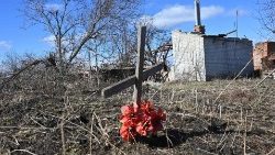Une croix dans un champ derrière une maison détruite en Ukraine