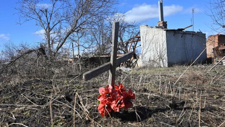 Una croce in un campo dietro una casa distrutta in Ucraina