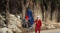 Nesta fotografia tirada em 9 de agosto de 2023, uma mulher afegã vestida de burca monta um burro junto com crianças em uma rua no distrito de Tagab, na província de Badakhshan. (Foto de OMER ABRAR/AFP)