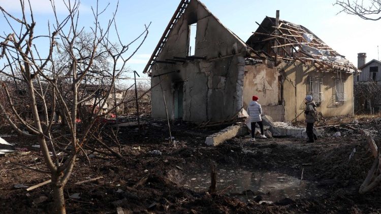 Crianças ficam ao lado de uma cratera em frente a uma casa destruída como resultado de um ataque de drone em Tairove (também escrito "Tayirove"), região de Odesa, em 17 de dezembro de 2023. (Foto de Anatolii STEPANOV / AFP)