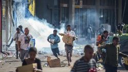Pessoas correm com mercadorias enquanto multidões saem das lojas com produtos saqueados em Port Moresby, em 10 de janeiro de 2024. (Foto da AFP)