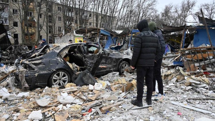 Moradores locais ficam ao lado de um carro destruído como resultado de um ataque com mísseis em Kharkiv, em 23 de janeiro de 2024, em meio à invasão russa da Ucrânia. (Foto de SERGEY BOBOK/AFP)