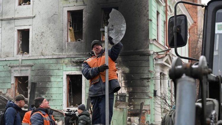 Trabalhadores comunitários limpam escombros espalhados pela rua em frente a um prédio danificado em Kharkiv, em 24 de janeiro de 2024, um dia depois de uma barragem de mísseis russos em todo o país. (Foto de SERGEY BOBOK/AFP)