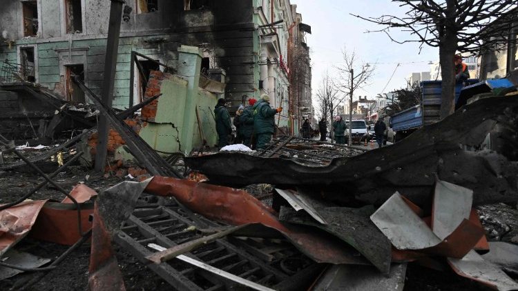 Trabalhadores comunitários limpam escombros espalhados pela rua em frente a um prédio danificado em Kharkiv, em 24 de janeiro de 2024, um dia depois de uma barragem de mísseis russos em todo o país. (Foto de SERGEY BOBOK/AFP)