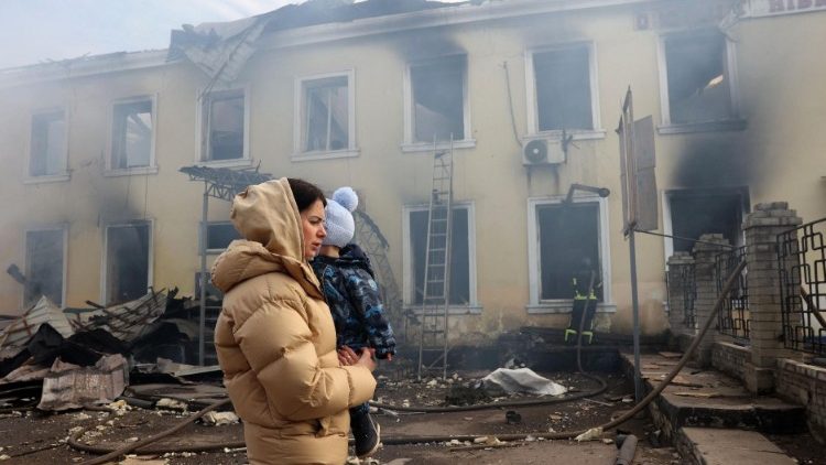 Residente local com criança no colo passa diante de estação de trem destruída por ataque russo em Konstyantynivka, região de Donetsk, em 25 de fevereiro de 2024. )Photo by Anatolii Stepanov/AFP)