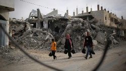 爆撃により破壊された建物の前を歩く人々　2024年3月3日　パレスチナ・ガザ地区ラファ