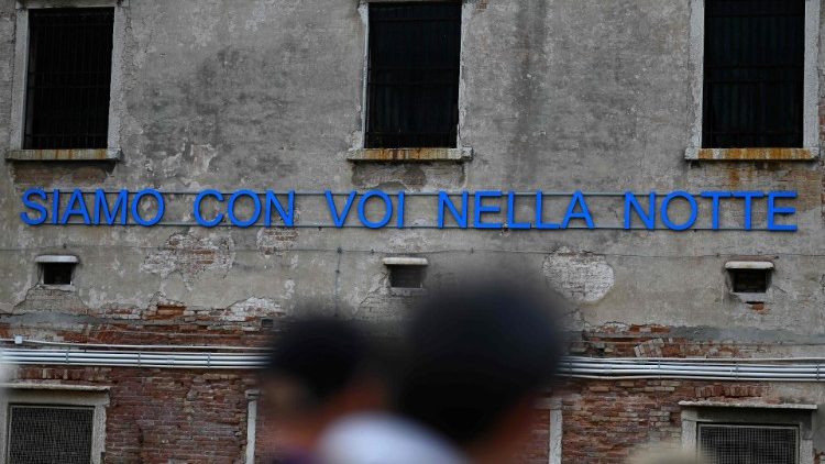 A sign reads "We are with you in the night" at the Holy See Pavilion in the Giudecca Prison