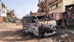 A burnt vehicle in front of damaged shop in Omdurman
