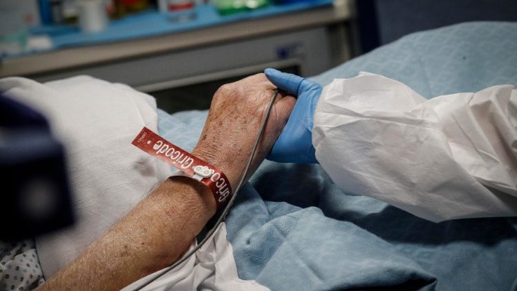 Một y tá nắm tay một bệnh nhân Covid-19 được điều trị trong phòng chăm sóc đặc biệt