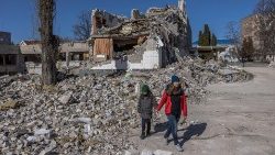 Ucraniana com seu filho diante de escola destruída por bombardeios russos em Zhytomyr, noroeste da Ucrânia