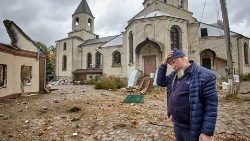 Ucraina. Un uomo davanti a una chiesa, a sinistra una abitazione distrutta