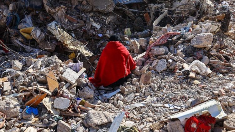 A woman sits on the rubble of her home where the bodies of her family members are still buried, in Hatay, Turkey